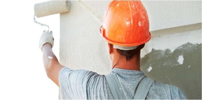 Personne peignant une façade avec un rouleau, portant un casque de sécurité.